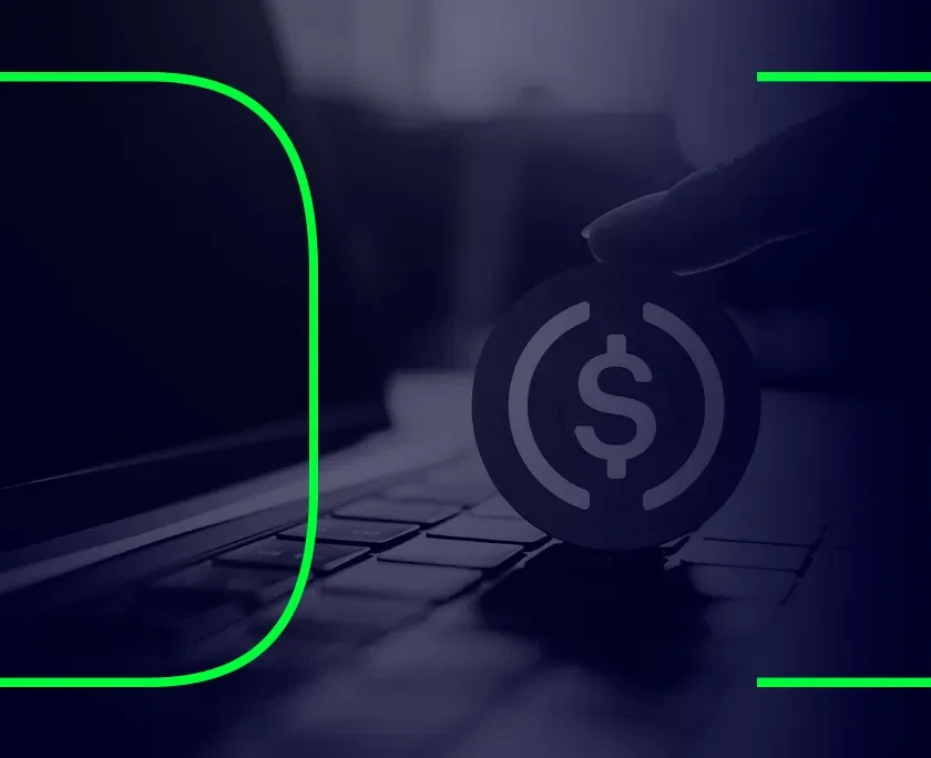 Foto em preto e branco de um computador com uma representação de uma moeda em cima do teclado, representando a USDC, stablecoin baseada no dólar americano