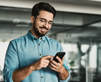 Pagamento Instantâneo - Foto de uma pessoa em ambiente corporativo mexendo no celular com uma expressão alegre